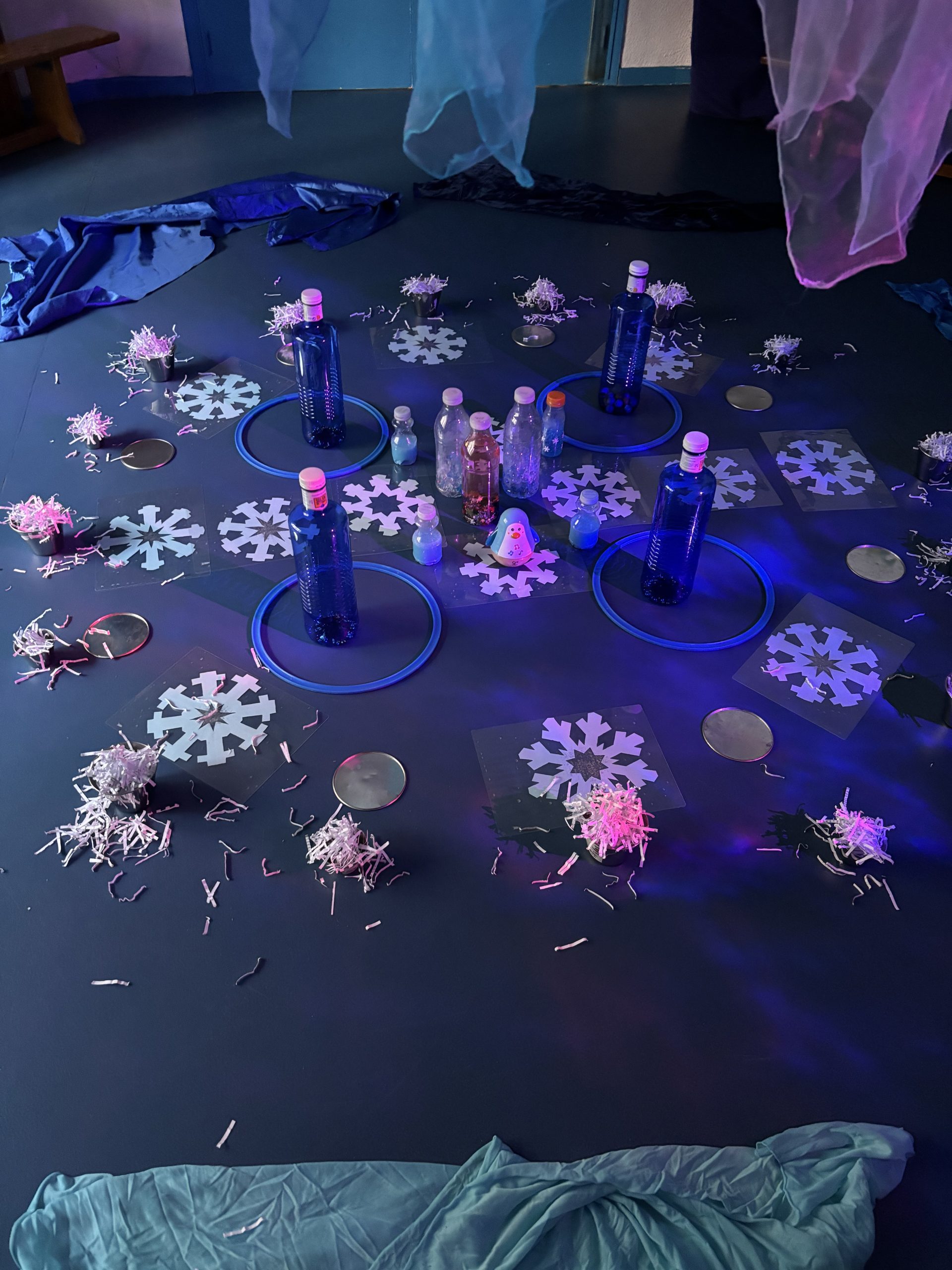 Detalle de botellas azules, purpurina y copos de nieve troquelados en el suelo.