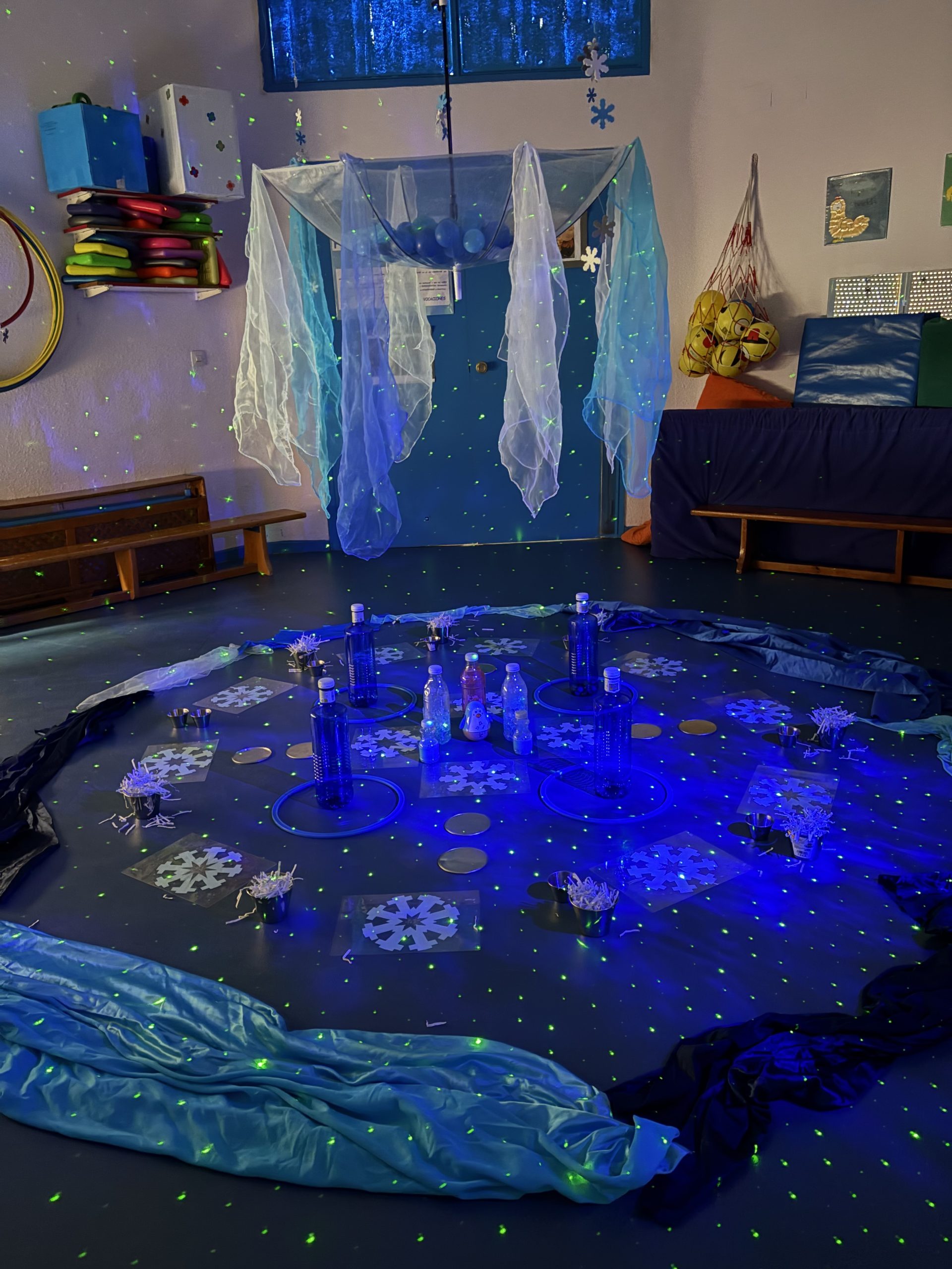 Aula a oscuras con motas de luz verde proyectadas sobre la instalación de invierno.